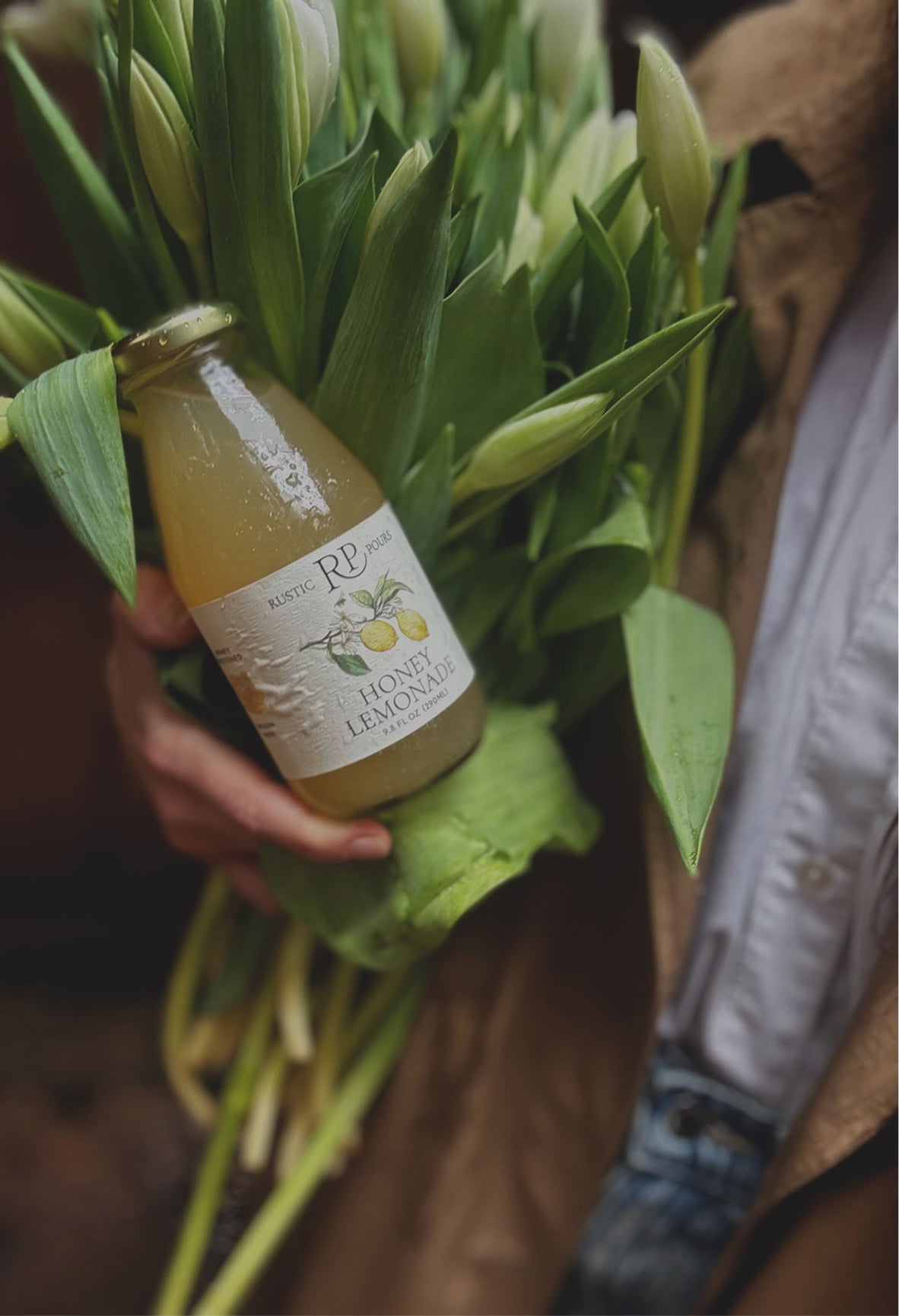 Hand holding a bottle of lemonade with a bouquet of flowers